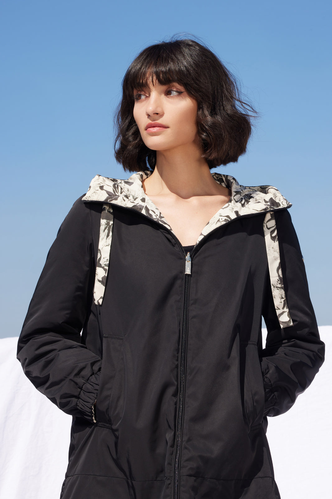 Geacă reversibilă Madzerini damă, neagră cu imprimeu floral alb-negru pe glugă.